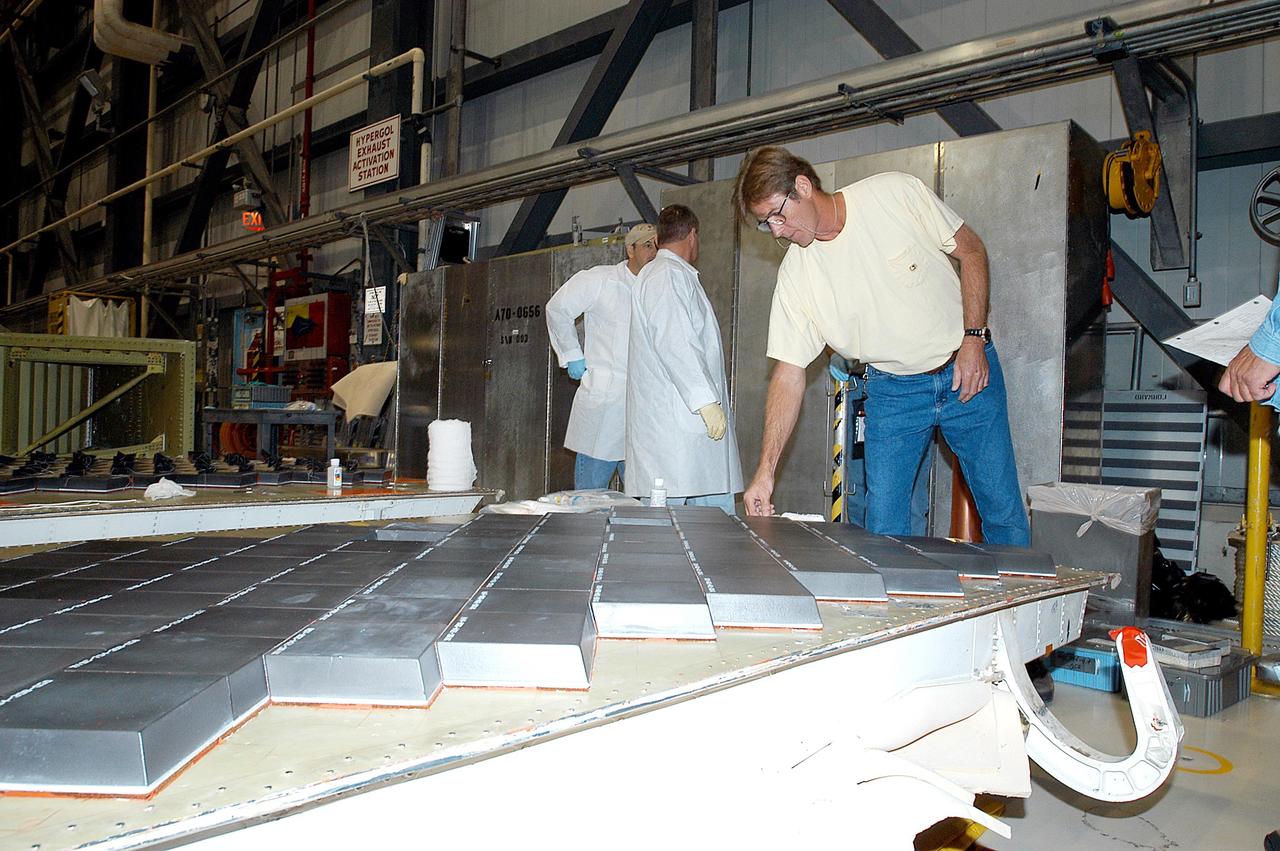 KENNEDY SPACE CENTER, FLA. -- In the Orbiter Processing Facility, United Space Alliance employee Harrell Watts (right) installs Thermal Protection System tiles on a main landing gear  door of Space Shuttle orbiter Enterprise (OV-101).  Sections of Enterprise were borrowed from the Smithsonian Institution's Air and Space Museum where the orbiter is being stored at the Washington Dulles International Airport.  Enterprise was the first orbiter built in the Shuttle fleet and was used to conduct the Approach and Landing Test Program before the first powered Shuttle flight.  After the tile installation is complete, the sections will be transferred to the Southwest Research Institute for testing requested by the Columbia Accident Investigation Board.