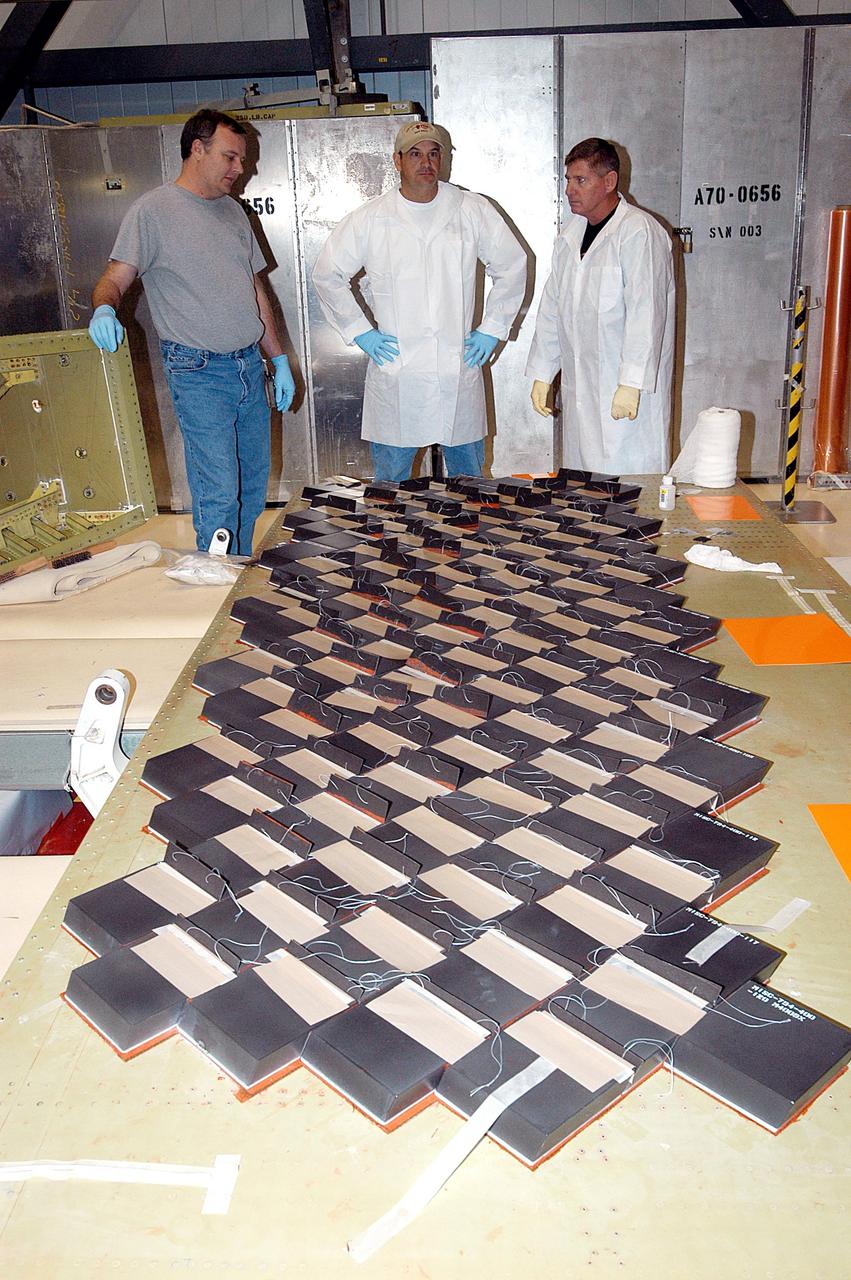 KENNEDY SPACE CENTER, FLA. -- In the Orbiter Processing Facility, United Space Alliance employees (from left) John Kuhn, Mike Cote, and Tom Baggitt discuss the installation of Thermal Protection System tiles on a main landing gear door of Space Shuttle orbiter Enterprise (OV-101).  Sections of Enterprise were borrowed from the Smithsonian Institution's Air and Space Museum where the orbiter is being stored at the Washington Dulles International Airport.  Enterprise was the first orbiter built in the Shuttle fleet and was used to conduct the Approach and Landing Test Program before the first powered Shuttle flight.  After the tile installation is complete, the sections will be transferred to the Southwest Research Institute for testing requested by the Columbia Accident Investigation Board.