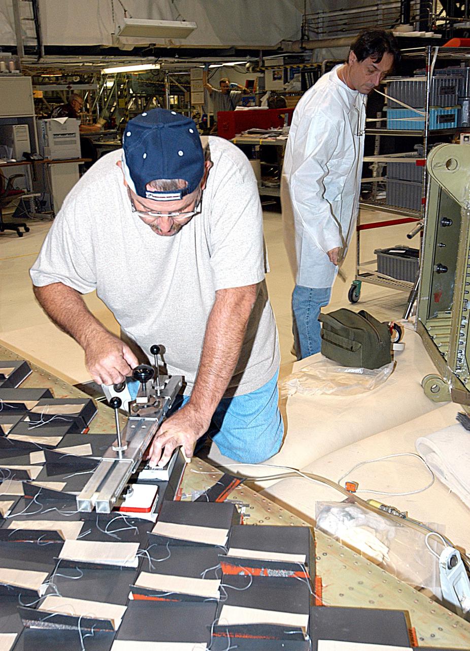 KENNEDY SPACE CENTER, FLA. -- In the Orbiter Processing Facility, United Space Alliance employee Dave Sanborn (left) conducts a bond verification test on Thermal Protection System tiles installed on a main landing gear door of Space Shuttle orbiter Enterprise (OV-101). Sections of Enterprise were borrowed from the Smithsonian Institution's Air and Space Museum where the orbiter is being stored at the Washington Dulles International Airport.  Enterprise was the first orbiter built in the Shuttle fleet and was used to conduct the Approach and Landing Test Program before the first powered Shuttle flight.  After the tile installation is complete, the sections will be transferred to the Southwest Research Institute for testing requested by the Columbia Accident Investigation Board.