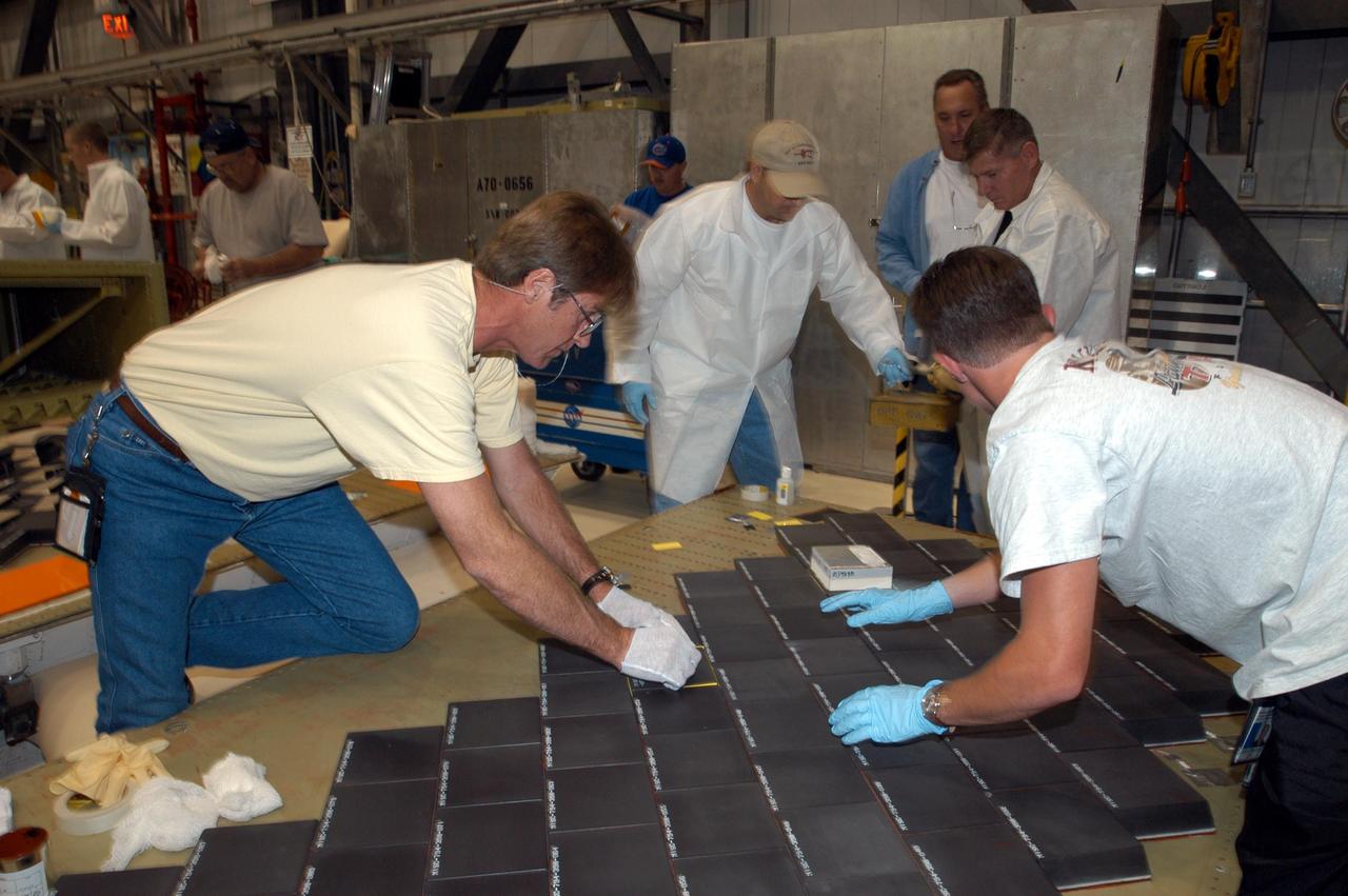 KENNEDY SPACE CENTER, FLA. -- In the Orbiter Processing Facility, United Space Alliance employees (from left)  Harrell Watts, Mike Cote, and Jason Levandusky install Thermal Protection System tiles on a main landing gear door of Space Shuttle orbiter Enterprise (OV-101).  Sections of Enterprise were borrowed from the Smithsonian Institution's Air and Space Museum where the orbiter is being stored at the Washington Dulles International Airport.  Enterprise was the first orbiter built in the Shuttle fleet and was used to conduct the Approach and Landing Test Program before the first powered Shuttle flight.  After the tile installation is complete, the sections will be transferred to the Southwest Research Institute for testing requested by the Columbia Accident Investigation Board.