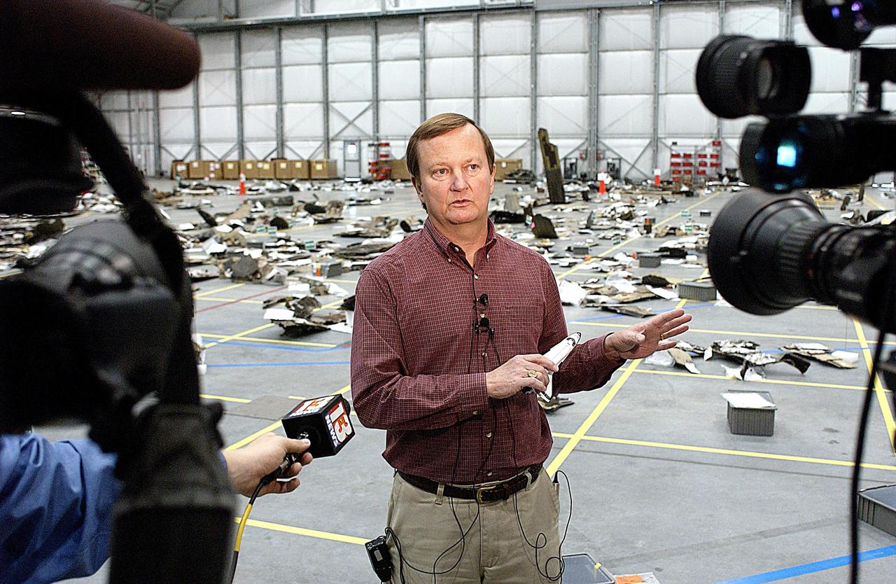 KENNEDY SPACE CENTER, FLA. -- Shuttle Launch Director Mike Leinbach answers reporters' questions in the RLV Hangar. Leinbach is overseeing assessment of the debris, seen in the background, as it is delivered to KSC. The Columbia Reconstruction Project team is identifying pieces and placing them on a grid approximating the shape of the orbiter. Shipped from Barksdale Air Force Base, Shreveport, La., more than 70,000 items, weighing 78,000 pounds, about 36 percent of the Shuttle by weight, have been delivered to KSC for use in the mishap investigation. Ground teams have completed 78 percent of their primary search area, and airborne crews finished 80 percent of their assigned area. Search teams have completed 98 percent of the underwater searches in Lake Nacogdoches and Toledo Bend Reservoir.