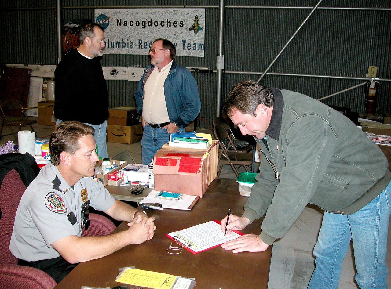 KENNEDY SPACE CENTER, FLA. -- Space Gateway Support Security Officer Jeff Ellison signs in a worker at the Nacogdoches site. In the background, NASA site lead Ronnie Lawson (left) speaks with his United Space Alliance counterpart George Odom. Kennedy Space Center workers are participating in the Columbia Recovery efforts at the Lufkin (Texas) Command Center, four field sites in East Texas, and the Barksdale, La., hangar site. KSC is working with representatives from other NASA Centers and with those from a number of federal, state and local agencies in the recovery effort. KSC provides vehicle technical expertise in the field to identify, collect and return Shuttle hardware to KSC.