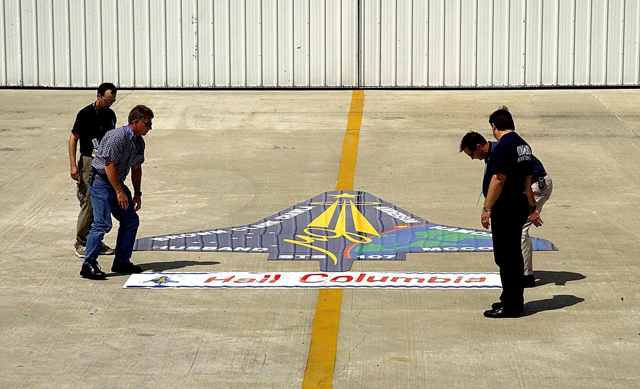 KENNEDY SPACE CENTER, FLA. -- Workers position a "Hail Columbia" banner beneath an enlarged replica of the STS-107 crew emblem at the RLV Hangar.  The emblem will be installed on an outside wall.  Inside the hangar, members of the Columbia Reconstruction Project team are identifying pieces of Columbia debris as they arrive at Kennedy Space Center and placing them on a grid approximating the shape of the orbiter.