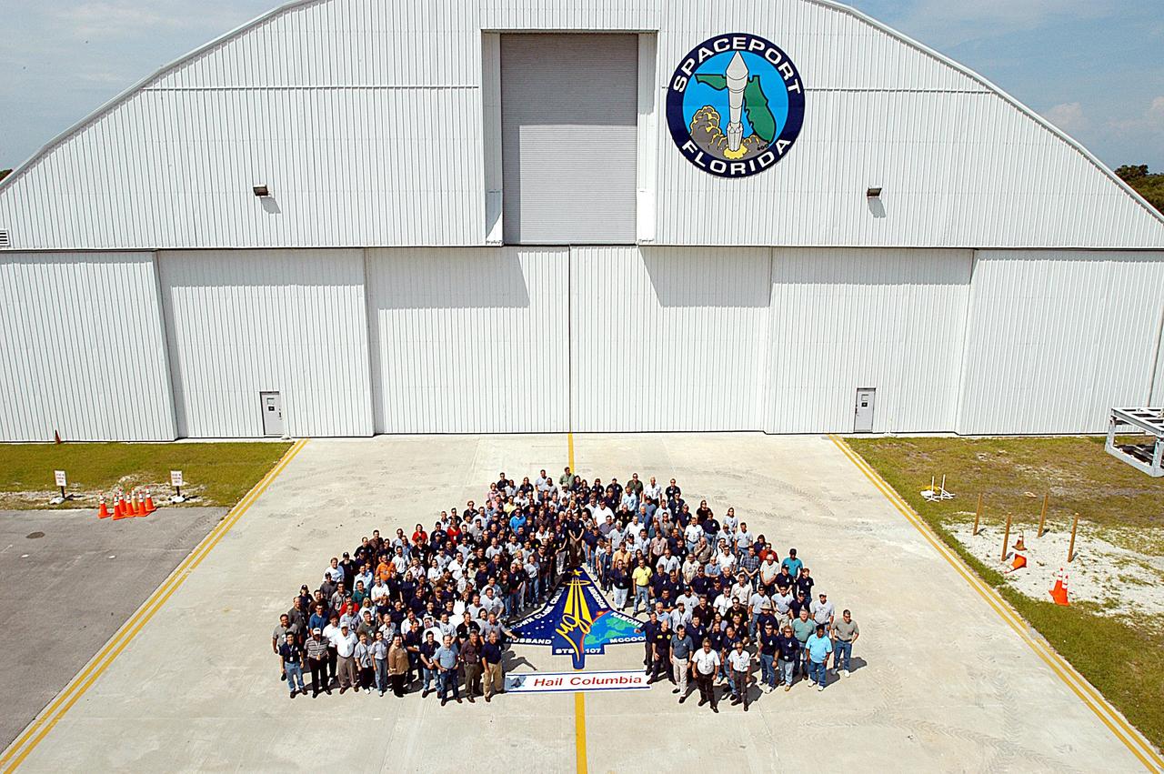 KENNEDY SPACE CENTER, FLA. -- Members of the Columbia Reconstruction Project team pose for a group photo around an enlarged replica of the STS-107 crew emblem just delivered to the RLV Hangar. The emblem will be installed on an outside wall of the hangar. Inside the hangar, the team is identifying pieces of Columbia debris as they arrive at Kennedy Space Center and placing them on a grid approximating the shape of the orbiter.