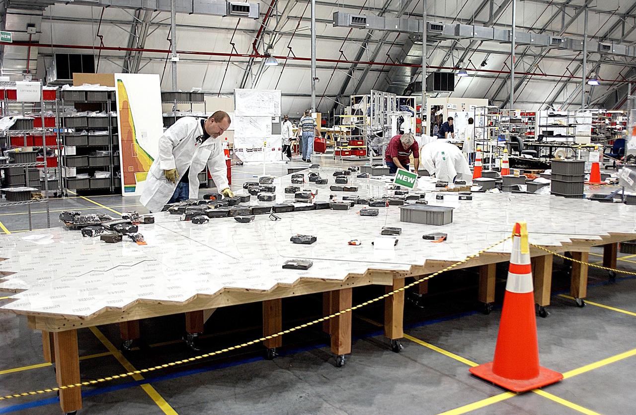 KENNEDY SPACE CENTER, FLA. --  In the RLV Hangar, members of the Columbia Reconstruction Project team place recovered Thermal Protection System (TPS) tile on a tabletop mock-up of the wing of Columbia. Shipped from Barksdale Air Force Base, Shreveport, La., more than 70,000 items, weighing 78,000 pounds, about 36 percent of the Shuttle by weight, have been delivered to KSC for use in the mishap investigation. Ground teams have completed 78 percent of their primary search area, and airborne crews finished 80 percent of their assigned area. Search teams have completed 98 percent of the underwater searches in Lake Nacogdoches and Toledo Bend Reservoir.