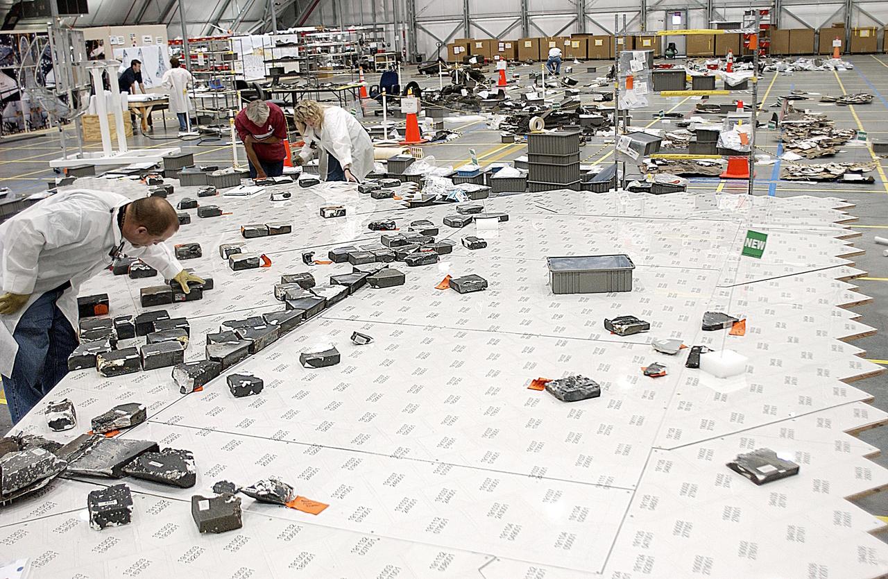 KENNEDY SPACE CENTER, FLA. --  In the RLV Hangar, members of the Columbia Reconstruction Project team place recovered Thermal Protection System (TPS) tile on a tabletop mock-up of the wing of Columbia. Shipped from Barksdale Air Force Base, Shreveport, La., more than 70,000 items, weighing 78,000 pounds, about 36 percent of the Shuttle by weight, have been delivered to KSC for use in the mishap investigation. Ground teams have completed 78 percent of their primary search area, and airborne crews finished 80 percent of their assigned area. Search teams have completed 98 percent of the underwater searches in Lake Nacogdoches and Toledo Bend Reservoir.