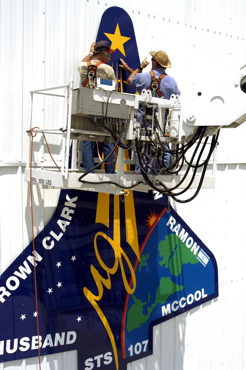 KENNEDY SPACE CENTER, FLA. - Workers place the final piece of the mission patch for STS-107 on the outside of the RLV Hangar at KSC.  The hangar is the site of the Columbia Reconstruction Project, where pieces of debris from Columbia are being collected and identified as part of the mishap investigation.