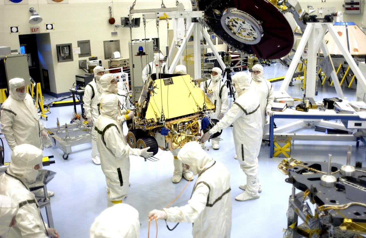 KENNEDY SPACE CENTER, FLA. - Workers in the Payload Hazardous Servicing Facility help guide the Mars Exploration Rover 1 (MER-1) as it is moved to the lander base petal for installation.  The MER Mission consists of two identical rovers, landing at different regions of Mars, designed to cover roughly 110 yards each Martian day over various terrain. Each rover will carry five scientific instruments that will allow it to search for evidence of liquid water that may have been present in the planet's past.  The first rover has a launch window opening June 5, and the second rover a window opening June 25. The rovers will be launched from Cape Canaveral Air Force Station.