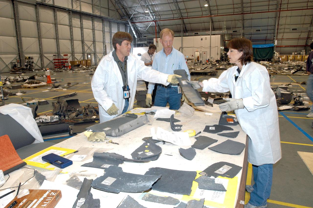 KENNEDY SPACE CENTER, FLA. - In the RLV Hangar, members of the Columbia Reconstruction Project Team look at several pieces of debris from Columbia.  More than 70,000 items have been delivered to KSC for use in the mishap investigation.  A portion of them sit on the floor within the grid and outline of Columbia.