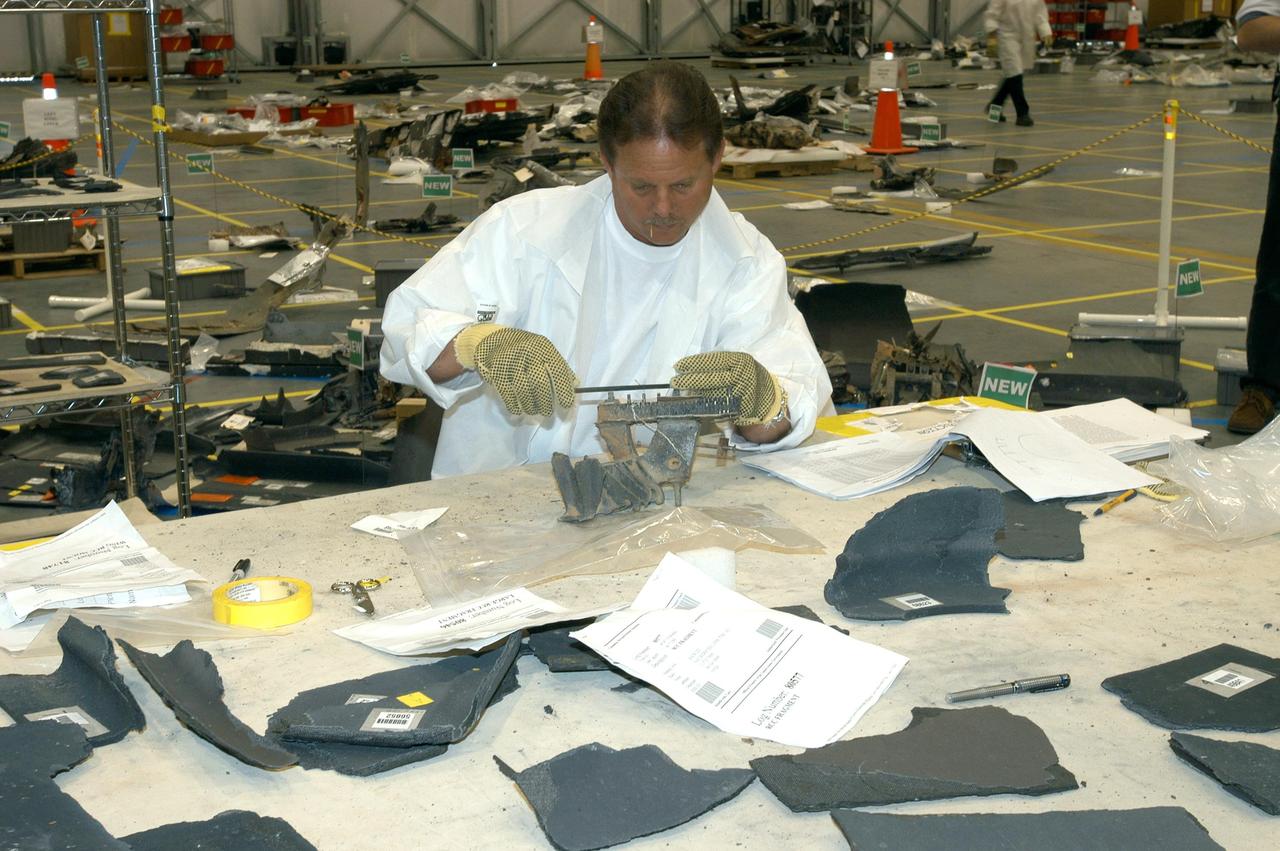 KENNEDY SPACE CENTER, FLA. - In the RLV Hangar, a member of the Columbia Reconstruction Project Team examines a piece of debris from Columbia.  More than 70,000 items have been delivered to KSC for use in the mishap investigation.  A portion of them sit on the floor within the grid and outline of Columbia.