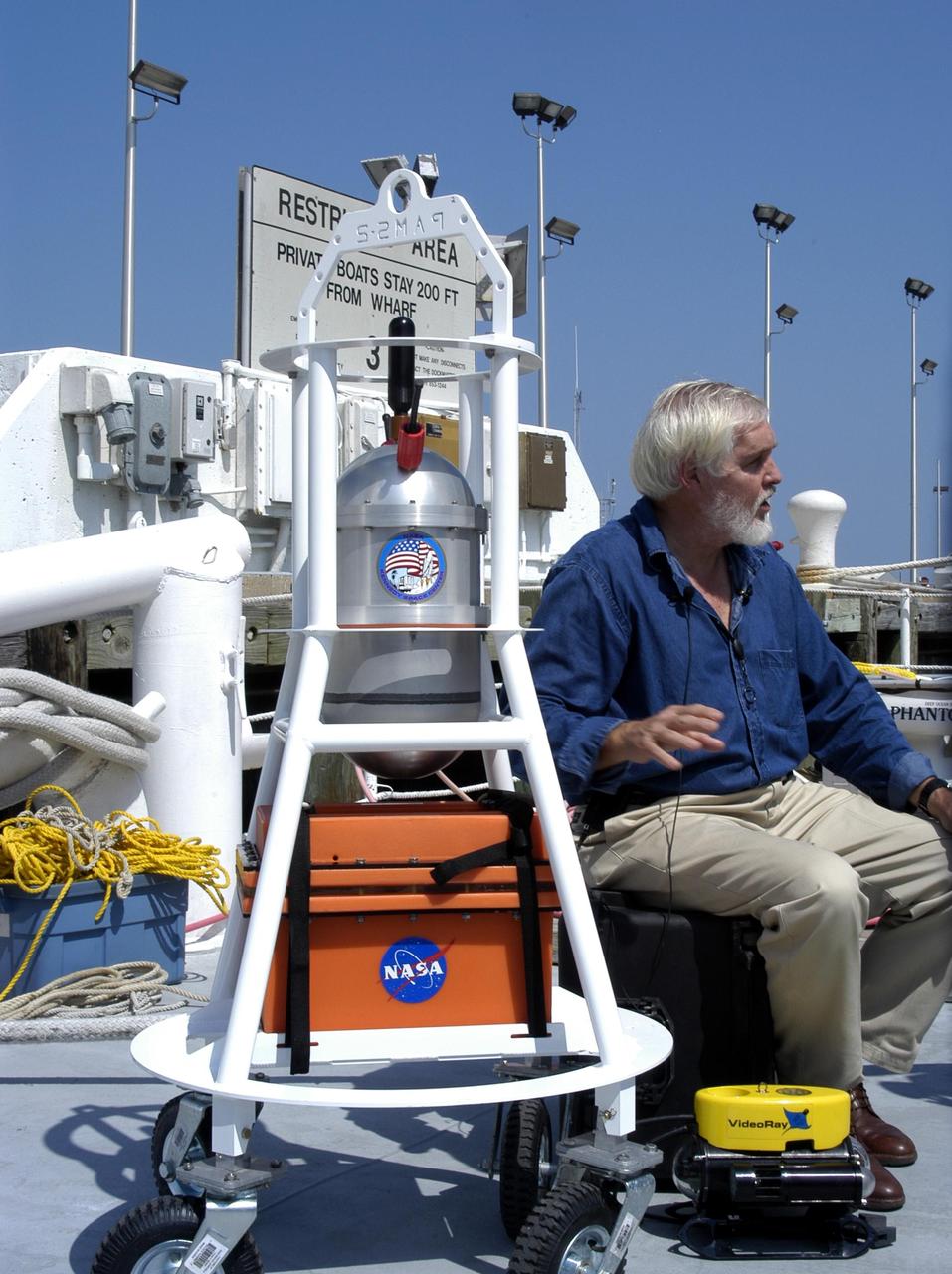 KENNEDY SPACE CENTER, FLA. - Dr. Grant Gilmore sits alongside some of the equipment that will be used on an undersea expedition to characterize the condition of the deep-sea coral reefs and reef fish populations in the Oculina Banks, a marine protected area, 20 miles offshore of the east coast of Florida. Scientists on the team will be deploying an underwater robot, a seafloor sampler, and the Passive Acoustic Monitoring System (PAMS). Gilmore is co-principle investigator of the PAMS, originally developed by NASA to monitor the impact of rocket launches on wildlife refuge lagoons at KSC. The research is sponsored by NOAA Fisheries and will take place onboard the Liberty Star. The ship departed from Port Canaveral April 29 and will return May 9.