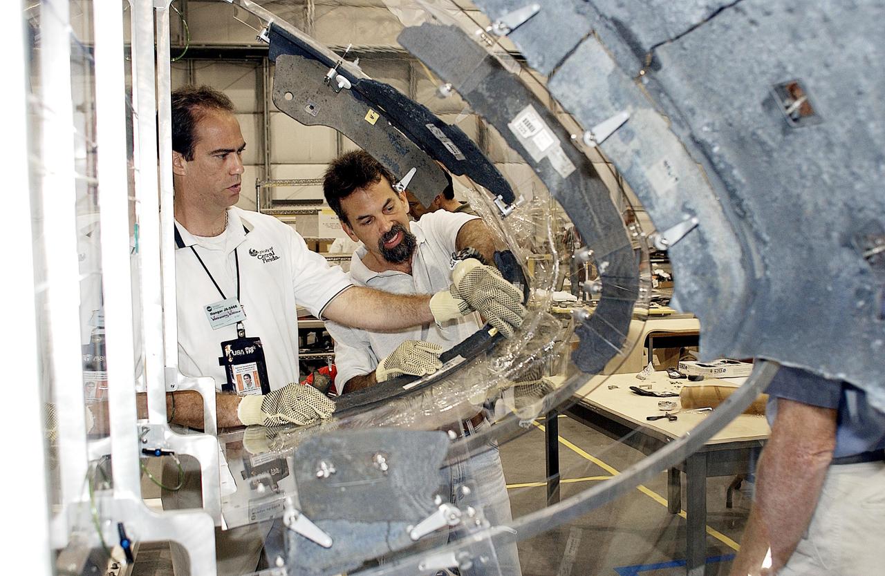 KENNEDY SPACE CENTER, FLA. - Members of the Columbia Reconstruction Project Team place debris on the mounting fixture for RCC pieces of the leading edge of Columbia's left wing. The final shipment of debris arrived on this date - recovery efforts have been concluded in East Texas. Prior to this final shipment, the total number of items at KSC is 82,567, weighing 84,800 pounds or 38 percent of the total dry weight of Columbia. Of those items, 78,760 have been identified, with 753 placed on the left wing grid in the RLV Hangar.