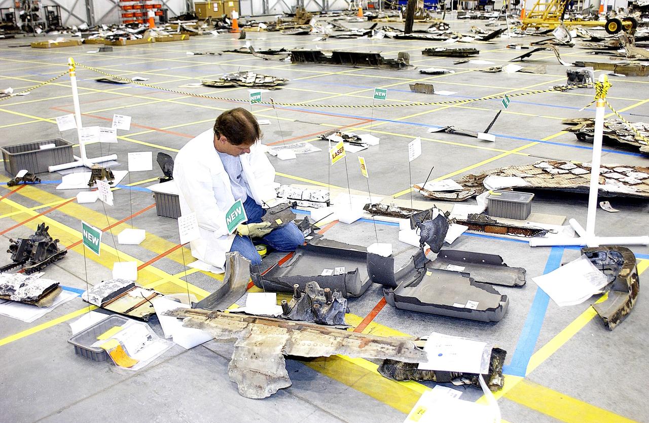 KENNEDY SPACE CENTER, FLA. - A member of the Columbia Reconstruction Project Team examines part of the Columbia debris on the floor of the RLV Hangar.  The final shipment of debris arrived on this date - recovery efforts have been concluded in East Texas.  Prior to this final shipment, the total number of items at KSC is 82,567, weighing 84,800 pounds or 38 percent of the total dry weight of Columbia.  Of those items, 78,760 have been identified, with 753 placed on the left wing grid in the RLV Hangar.