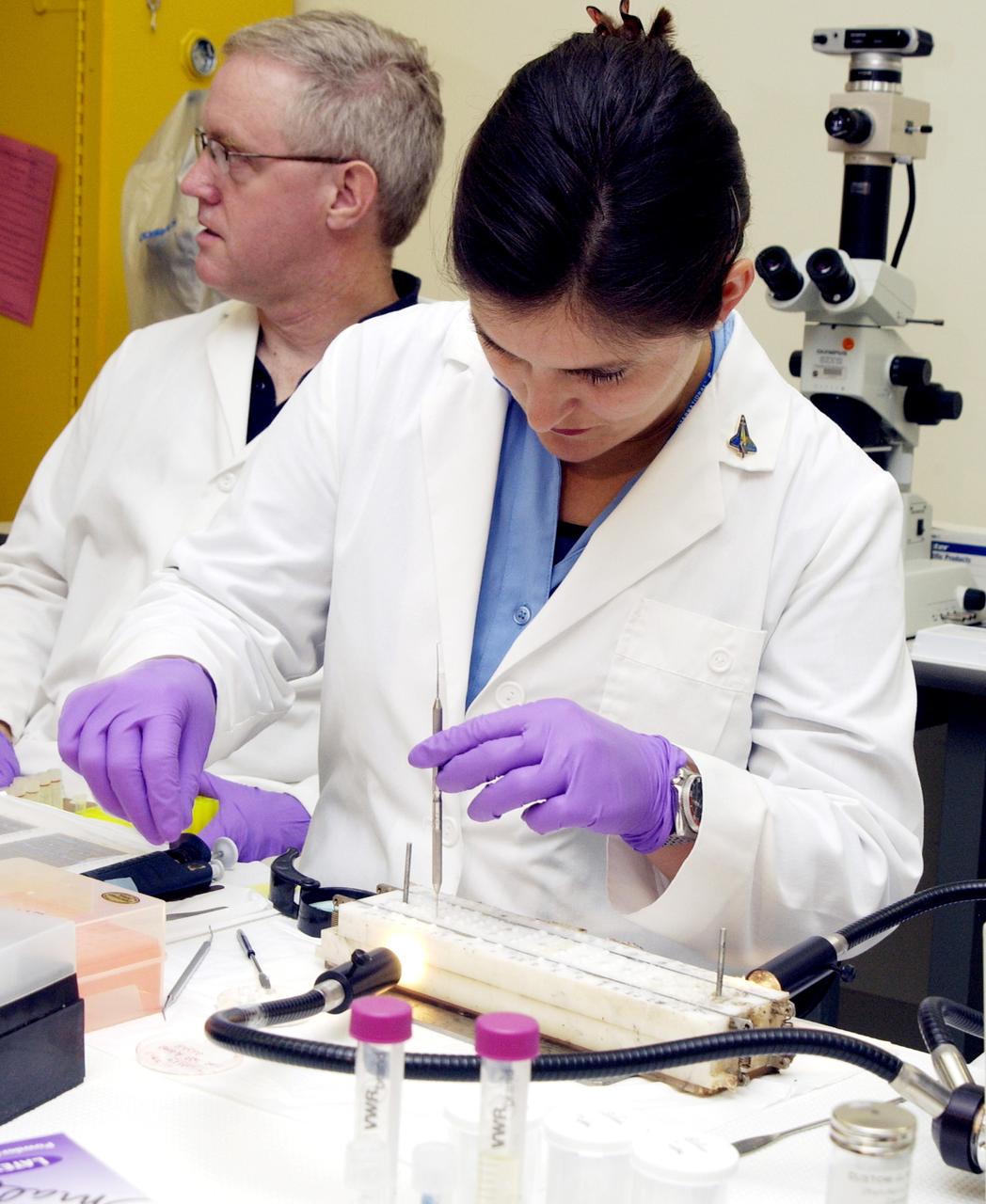 KENNEDY SPACE CENTER, FLA. -  Valerie Cassanto (foreground), Instrumentation Technology Associates, Inc., examines one of the experiments carried on mission STS-107. Several experiments were found during the search for Columbia debris. Included in the Commercial ITA Biomedical Experiments payload on mission STS-107 are urokinase cancer research, microencapsulation of drugs, the Growth of Bacterial Biofilm on Surfaces during Spaceflight (GOBBSS), and tin crystal formation.