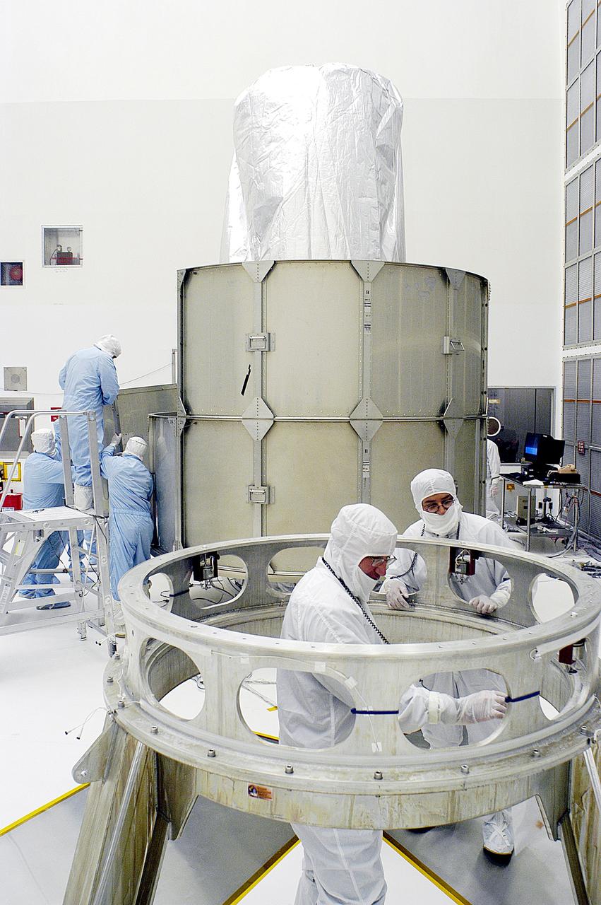 KENNEDY SPACE CENTER, FLA. -  Workers in NASA Spacecraft Hangar AE (background) remove sections of the transportation canister from around the Space Infrared Telescope Facility (SIRTF), which has been returned to the hangar from the launch pad.   Additional workers (foreground) prepare the Delta payload attach fitting, from which SIRTF was demated, for further use.  SIRTF will remain in the clean room until it returns to the pad in early August. One of NASA's largest infrared telescopes to be launched, SIRTF will obtain images and spectra by detecting the infrared energy, or heat, radiated by objects in space.