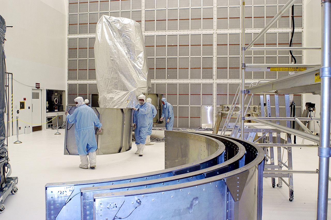 KENNEDY SPACE CENTER, FLA. -  Workers in NASA Spacecraft Hangar AE remove sections of the transportation canister from around the Space Infrared Telescope Facility (SIRTF), which has been returned to the hangar from the launch pad.   SIRTF will remain in the clean room until it returns to the pad in early August. One of NASA's largest infrared telescopes to be launched, SIRTF will obtain images and spectra by detecting the infrared energy, or heat, radiated by objects in space.