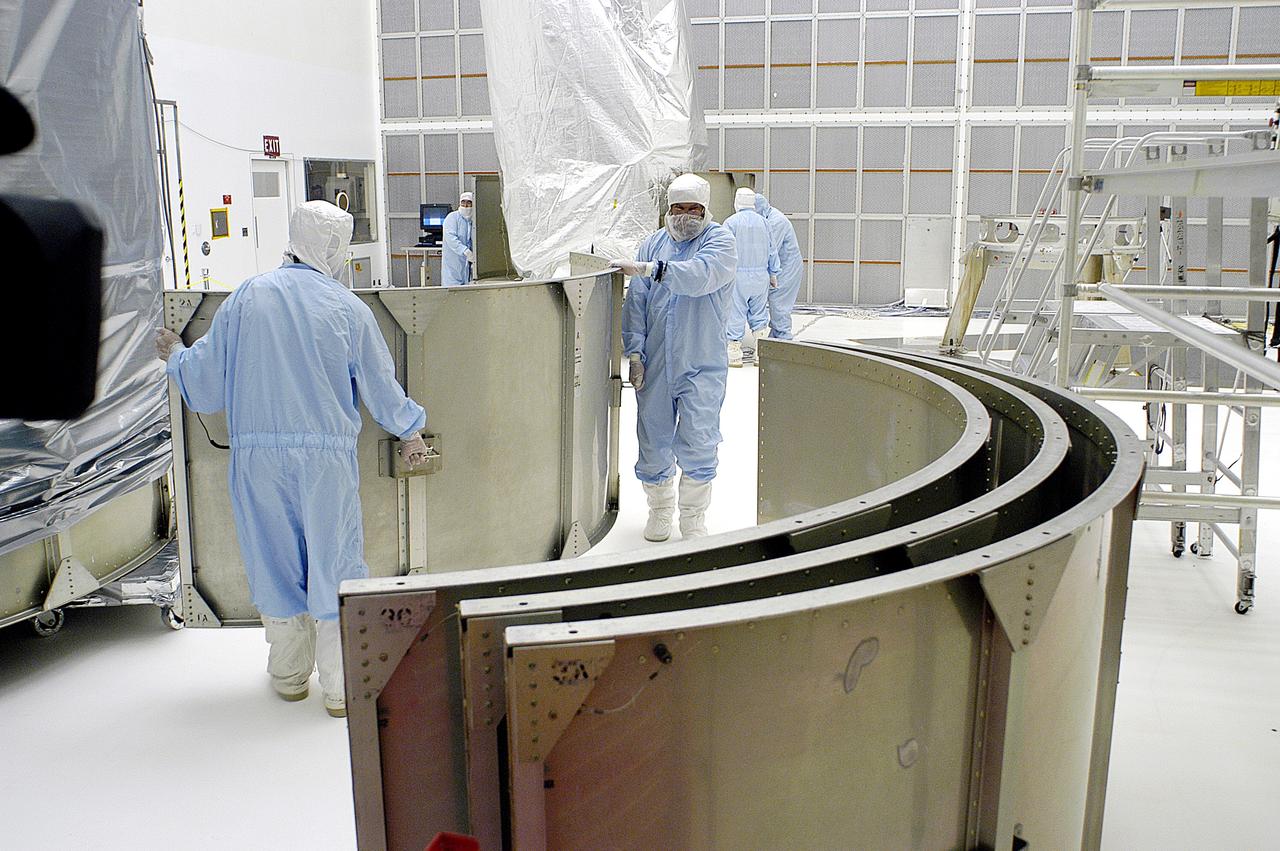 KENNEDY SPACE CENTER, FLA. -  Workers in NASA Spacecraft Hangar AE remove sections of the transportation canister from around the Space Infrared Telescope Facility (SIRTF), which has been returned to the hangar from the launch pad.   SIRTF will remain in the clean room until it returns to the pad in early August. One of NASA's largest infrared telescopes to be launched, SIRTF will obtain images and spectra by detecting the infrared energy, or heat, radiated by objects in space.