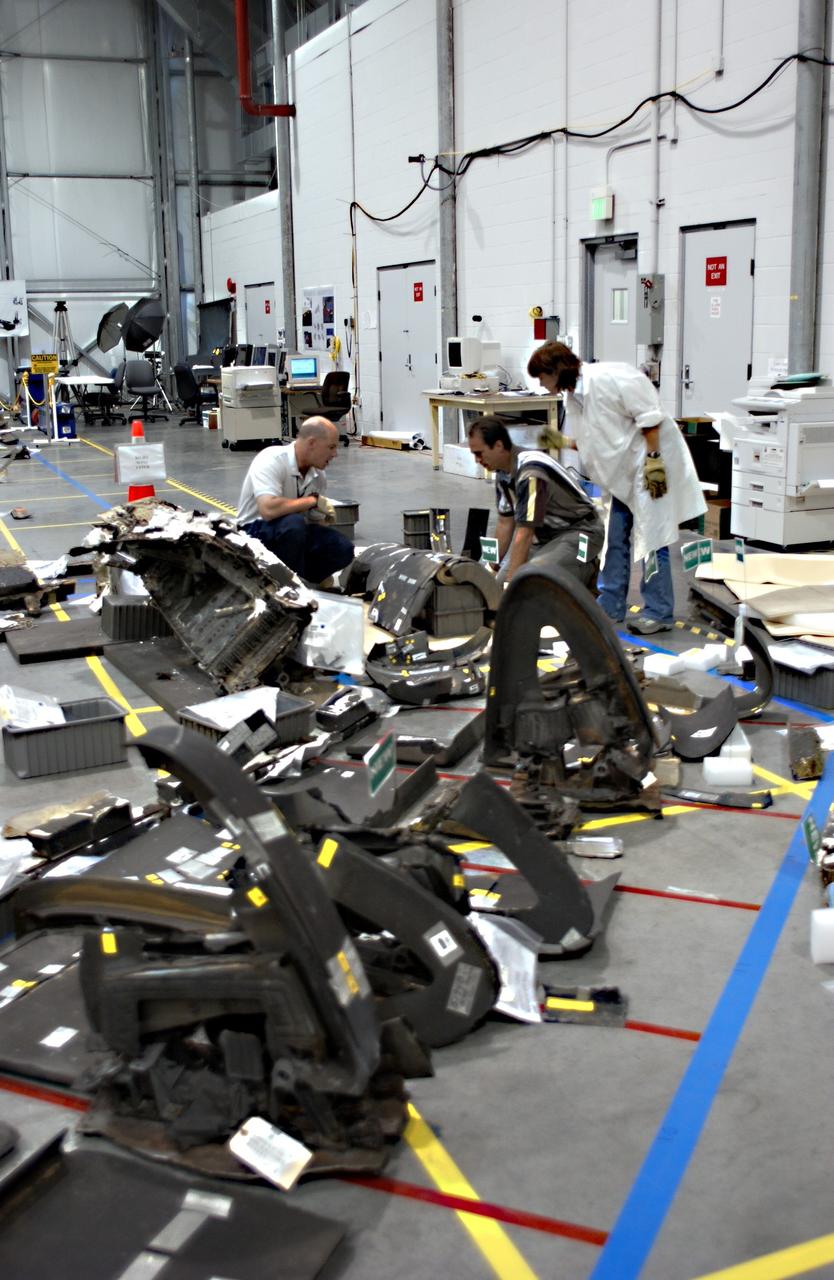 KENNEDY SPACE CENTER, FLA. - Members of the Columbia Reconstruction Project Team place a piece of debris from Columbia on the grid of the floor of the RLV Hangar.   The items at KSC number more than 82,000, weigh 84,800 pounds or 38 percent of the total dry weight of Columbia.  Of those items, 78,760 have been identified, with 753 placed on the left wing grid in the RLV Hangar.