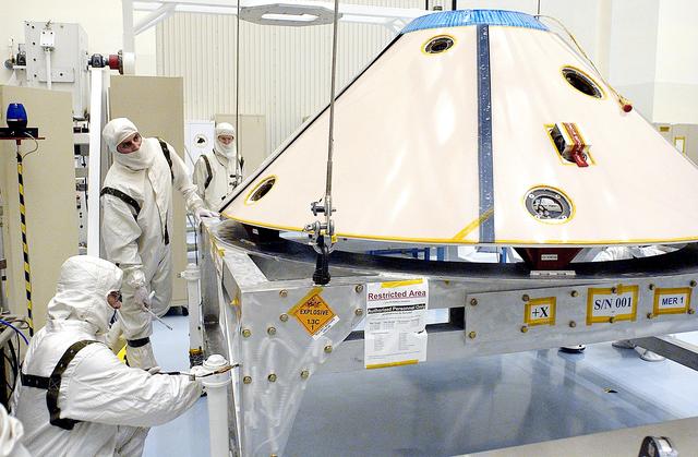 NASA image: KENNEDY SPACE CENTER, FLA. - Workers in the Payload Hazardous Servicing Facility prepare to lift and move the backshell, a protective cover for the Mars Exploration Rover 1 (MER-1) and its lander.  NASA's twin Mars Exploration Rovers are designed to study the history of water on Mars. These robotic geologists are equipped with a robotic arm, a drilling tool, three spectrometers, and four pairs of cameras that allow them to have a human-like, 3D view of the terrain. Each rover could travel as far as 100 meters in one day to act as Mars scientists' eyes and hands, exploring an environment where humans can't yet go.  MER-1 is scheduled to launch June 25 as MER-B aboard a Delta II rocket from Cape Canaveral Air Force Station.