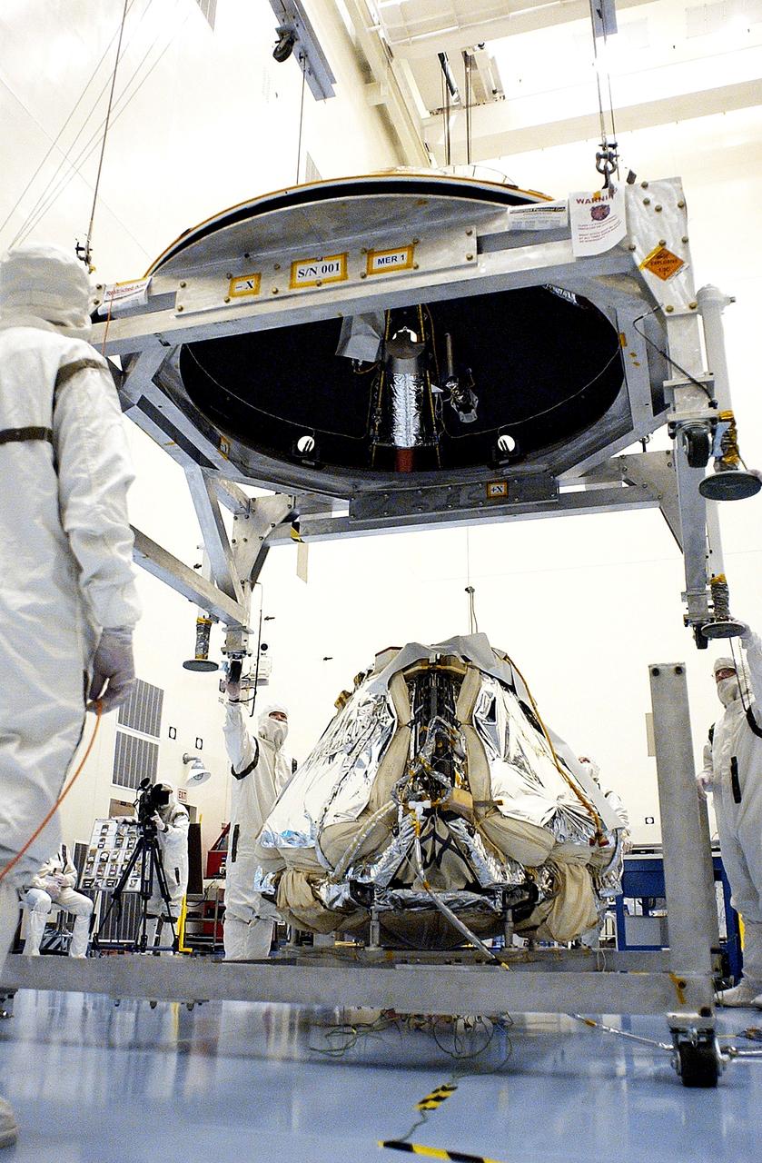 KENNEDY SPACE CENTER, FLA. - Workers in the Payload Hazardous Servicing Facility lower the backshell over the Mars Exploration Rover 1 (MER-1).  The backshell is a protective cover for the rover.  NASA's twin Mars Exploration Rovers are designed to study the history of water on Mars. These robotic geologists are equipped with a robotic arm, a drilling tool, three spectrometers, and four pairs of cameras that allow them to have a human-like, 3D view of the terrain. Each rover could travel as far as 100 meters in one day to act as Mars scientists' eyes and hands, exploring an environment where humans can't yet go.  MER-1 is scheduled to launch June 25 as MER-B aboard a Delta II rocket from Cape Canaveral Air Force Station.