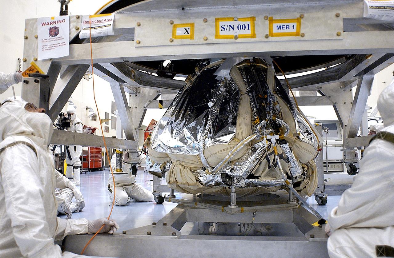 KENNEDY SPACE CENTER, FLA. - Workers in the Payload Hazardous Servicing Facility lower the backshell over the Mars Exploration Rover 1 (MER-1).  The backshell is a protective cover for the rover.  NASA's twin Mars Exploration Rovers are designed to study the history of water on Mars. These robotic geologists are equipped with a robotic arm, a drilling tool, three spectrometers, and four pairs of cameras that allow them to have a human-like, 3D view of the terrain. Each rover could travel as far as 100 meters in one day to act as Mars scientists' eyes and hands, exploring an environment where humans can't yet go.  MER-1 is scheduled to launch June 25 as MER-B aboard a Delta II rocket from Cape Canaveral Air Force Station.
