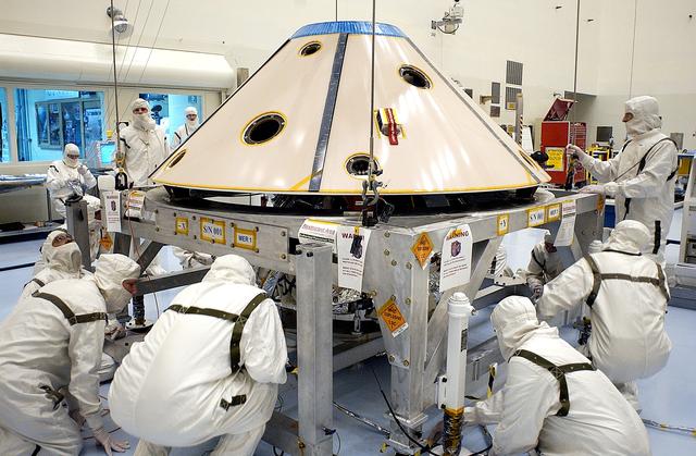 NASA image: KENNEDY SPACE CENTER, FLA. - Workers in the Payload Hazardous Servicing Facility check the placement of the backshell over the Mars Exploration Rover 1 (MER-1).  The backshell is a protective cover for the rover.  NASA's twin Mars Exploration Rovers are designed to study the history of water on Mars. These robotic geologists are equipped with a robotic arm, a drilling tool, three spectrometers, and four pairs of cameras that allow them to have a human-like, 3D view of the terrain. Each rover could travel as far as 100 meters in one day to act as Mars scientists' eyes and hands, exploring an environment where humans can't yet go.  MER-1 is scheduled to launch June 25 as MER-B aboard a Delta II rocket from Cape Canaveral Air Force Station.