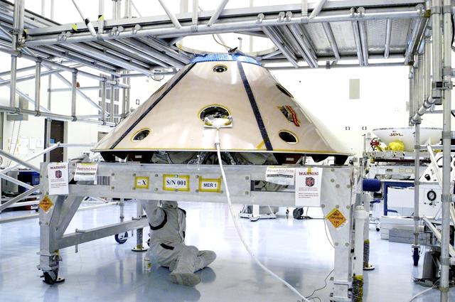 NASA image: KENNEDY SPACE CENTER, FLA. - Workers in the Payload Hazardous Servicing Facility check the installation of the Mars Exploration Rover 1 (MER-1) inside the upper backshell.   The two components will be attached to the lower heat shield.  NASA's twin Mars Exploration Rovers are designed to study the history of water on Mars. These robotic geologists are equipped with a robotic arm, a drilling tool, three spectrometers, and four pairs of cameras that allow them to have a human-like, 3D view of the terrain. Each rover could travel as far as 100 meters in one day to act as Mars scientists' eyes and hands, exploring an environment where humans can't yet go.  MER-1 is scheduled to launch June 25 as MER-B aboard a Delta II rocket from Cape Canaveral Air Force Station.