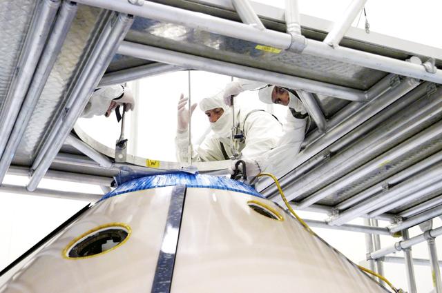 NASA image: KENNEDY SPACE CENTER, FLA. -  Workers attach an overhead crane to the Mars Exploration Rover 1 (MER-1) inside the upper backshell.   The backshell will be moved and attached to the lower heat shield.  NASA's twin Mars Exploration Rovers are designed to study the history of water on Mars. These robotic geologists are equipped with a robotic arm, a drilling tool, three spectrometers, and four pairs of cameras that allow them to have a human-like, 3D view of the terrain. Each rover could travel as far as 100 meters in one day to act as Mars scientists' eyes and hands, exploring an environment where humans can't yet go.  MER-1 is scheduled to launch June 25 as MER-B aboard a Delta II rocket from Cape Canaveral Air Force Station.