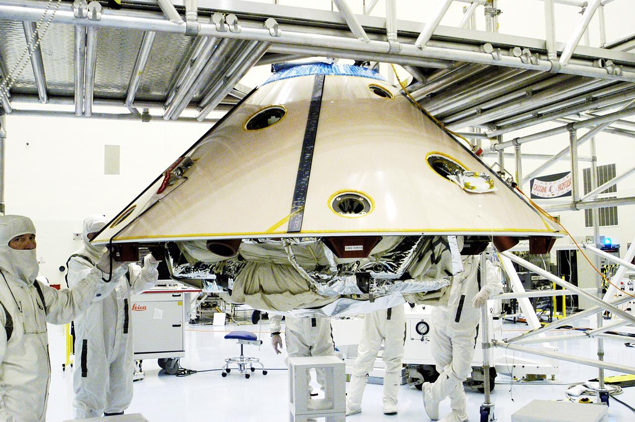 KENNEDY SPACE CENTER, FLA. - Workers walk with the suspended backshell/ Mars Exploration Rover 1 (MER-1) as it travels across the floor of the Payload Hazardous Servicing Facility.  The backshell will be attached to the lower heat shield.  NASA's twin Mars Exploration Rovers are designed to study the history of water on Mars. These robotic geologists are equipped with a robotic arm, a drilling tool, three spectrometers, and four pairs of cameras that allow them to have a human-like, 3D view of the terrain. Each rover could travel as far as 100 meters in one day to act as Mars scientists' eyes and hands, exploring an environment where humans can't yet go.  MER-1 is scheduled to launch June 25 as MER-B aboard a Delta II rocket from Cape Canaveral Air Force Station.