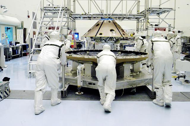 NASA image: KENNEDY SPACE CENTER, FLA. - In the Payload Hazardous Servicing Facility, workers move the heat shield (foreground) toward the upper backshell/ Mars Exploration Rover 1 (MER-1), in the background.  The backshell and heat shield will be mated.  NASA's twin Mars Exploration Rovers are designed to study the history of water on Mars. These robotic geologists are equipped with a robotic arm, a drilling tool, three spectrometers, and four pairs of cameras that allow them to have a human-like, 3D view of the terrain. Each rover could travel as far as 100 meters in one day to act as Mars scientists' eyes and hands, exploring an environment where humans can't yet go.  MER-1 is scheduled to launch June 25 as MER-B aboard a Delta II rocket from Cape Canaveral Air Force Station.