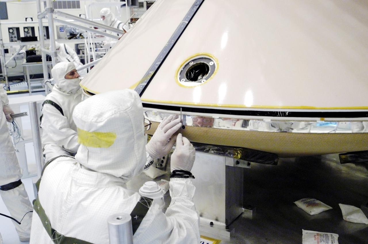 KENNEDY SPACE CENTER, FLA. - In the Payload Hazardous Servicing Facility, workers check the attachment between the backshell (above) and heat shield (below) surrounding the Mars Exploration Rover 1 (MER-1).  The aeroshell will protect the rover on its journey to Mars.  NASA's twin Mars Exploration Rovers are designed to study the history of water on Mars. These robotic geologists are equipped with a robotic arm, a drilling tool, three spectrometers, and four pairs of cameras that allow them to have a human-like, 3D view of the terrain. Each rover could travel as far as 100 meters in one day to act as Mars scientists' eyes and hands, exploring an environment where humans can't yet go.  MER-1 is scheduled to launch June 25 as MER-B aboard a Delta II rocket from Cape Canaveral Air Force Station.