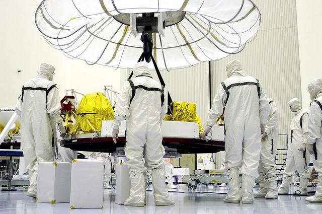 NASA image: KENNEDY SPACE CENTER, FLA. - In the Payload Hazardous Servicing Facility, workers stand by while an overhead crane again lifts the cruise stage of Mars Exploration Rover 1 (MER-1).  The cruise stage will be integrated with the aeroshell, the entry vehicle.   NASA’s twin Mars Exploration Rovers are designed to study the history of water on Mars. These robotic geologists are equipped with a robotic arm, a drilling tool, three spectrometers, and four pairs of cameras that allow them to have a human-like, 3D view of the terrain. Each rover could travel as far as 100 meters in one day to act as Mars scientists' eyes and hands, exploring an environment where humans can’t yet go.  The MER-1 is scheduled to launch June 25 from Launch Pad 17-A, Cape Canaveral Air Force Station.