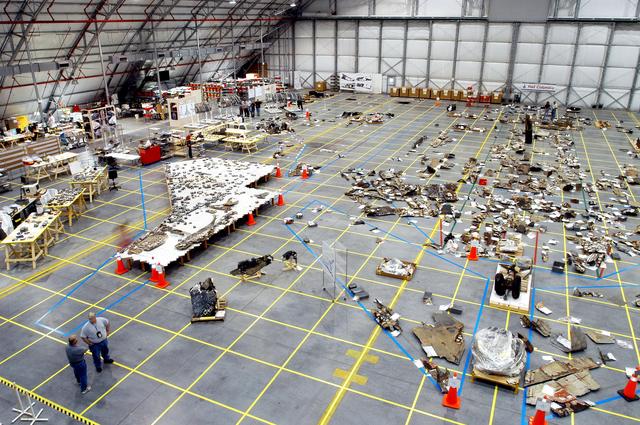 NASA image: KENNEDY SPACE CENTER, FLA. - An overview of the Columbia debris hangar shows the orbiter outline on the floor with some of the 78,760 pieces identified to date, as well as tables on the left that hold tiles.  More than 82,500 pieces of shuttle debris have been rcovered.