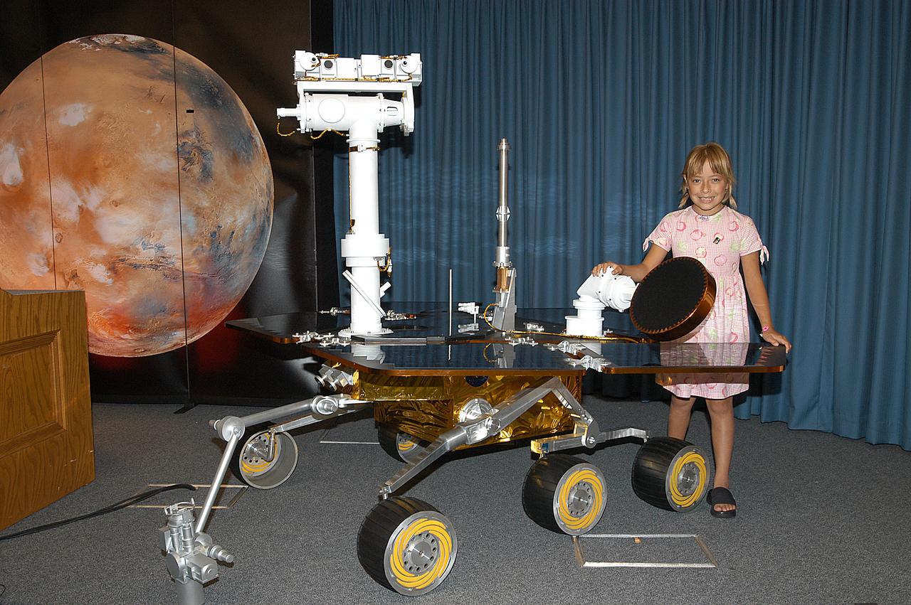 Sofi Collis, the third grade student winner of the "Name the Rovers" contest, poses with a model of a rover. The names she proposed -- Spirit and Opportunity -- were announced today in a press conference held by NASA Administrator Sean O'Keefe. NASA's twin Mars Exploration Rovers are designed to study the history of water on Mars. These robotic geologists are equipped with a robotic arm, a drilling tool, three spectrometers, and four pairs of cameras that allow them to have a human-like, 3D view of the terrain. Each rover could travel as far as 100 meters in one day to act as Mars scientists' eyes and hands, exploring an environment where humans are not yet able to go. MER-A, with the rover Spirit aboard, is scheduled to launch on June 8 at 2:06 p.m. EDT, with two launch opportunities each day during a launch period that closes on June 24.