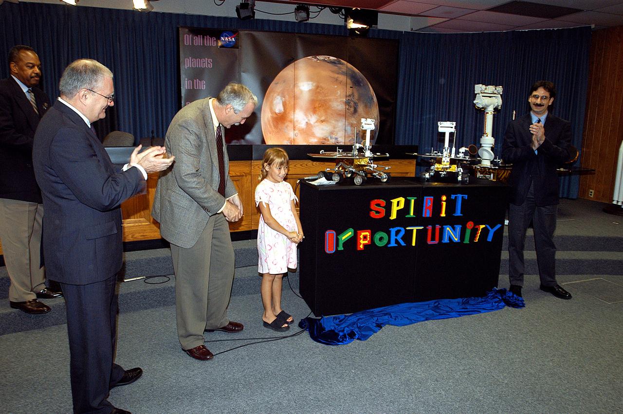KENNEDY SPACE CENTER, FLA. -  Nine-year-old Sofi Collis unveils the names of the Mars Exploration Rovers  -- "Spirit" and "Opportunity" --  during a press conference.  Participating in the press conference are, from left, Dr. John Marburger, science advisor to the President and director of the Office of Science and Technology Policy; NASA Administrator Sean O'Keefe; Sofi Collis, a third grade student from Arizona; and Brad Justus, LEGO Co. senior vice president.  The names Sofi suggested were selected from more than 10,000 student entries in an essay contest managed for NASA by the LEGO Company.   NASA's twin Mars Exploration Rovers are designed to study the history of water on Mars. These robotic geologists are equipped with a robotic arm, a drilling tool, three spectrometers, and four pairs of cameras that allow them to have a human-like, 3D view of the terrain. Each rover could travel as far as 100 meters in one day to act as Mars scientists' eyes and hands, exploring an environment where humans are not yet able to go. MER-A, with the rover Spirit aboard, is scheduled to launch on June 8 at 2:06 p.m. EDT, with two launch opportunities each day during a launch period that closes on June 24.