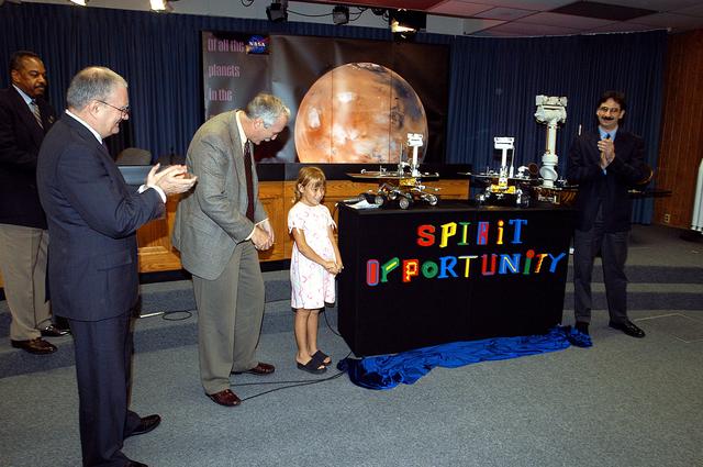 NASA image: KENNEDY SPACE CENTER, FLA. -  Nine-year-old Sofi Collis unveils the names of the Mars Exploration Rovers  -- "Spirit" and "Opportunity" --  during a press conference.  Participating in the press conference are, from left, Dr. John Marburger, science advisor to the President and director of the Office of Science and Technology Policy; NASA Administrator Sean O'Keefe; Sofi Collis, a third grade student from Arizona; and Brad Justus, LEGO Co. senior vice president.  The names Sofi suggested were selected from more than 10,000 student entries in an essay contest managed for NASA by the LEGO Company.   NASA's twin Mars Exploration Rovers are designed to study the history of water on Mars. These robotic geologists are equipped with a robotic arm, a drilling tool, three spectrometers, and four pairs of cameras that allow them to have a human-like, 3D view of the terrain. Each rover could travel as far as 100 meters in one day to act as Mars scientists' eyes and hands, exploring an environment where humans are not yet able to go. MER-A, with the rover Spirit aboard, is scheduled to launch on June 8 at 2:06 p.m. EDT, with two launch opportunities each day during a launch period that closes on June 24.