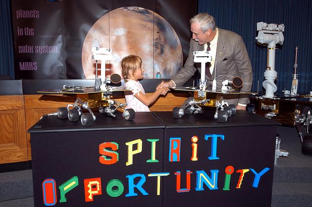NASA image: KENNEDY SPACE CENTER, FLA. -  Nine-year-old Sofi Collis (left) is congratulated by NASA Administrator Sean O'Keefe for selecting the names of the Mars Exploration Rovers  -- "Spirit" and "Opportunity" --  during a press conference.  The names Sofi suggested were chosen from more than 10,000 student entries in an essay contest managed for NASA by the LEGO Company.   NASA's twin Mars Exploration Rovers are designed to study the history of water on Mars. These robotic geologists are equipped with a robotic arm, a drilling tool, three spectrometers, and four pairs of cameras that allow them to have a human-like, 3D view of the terrain. Each rover could travel as far as 100 meters in one day to act as Mars scientists' eyes and hands, exploring an environment where humans are not yet able to go. MER-A, with the rover Spirit aboard, is scheduled to launch on June 8 at 2:06 p.m. EDT, with two launch opportunities each day during a launch period that closes on June 24.