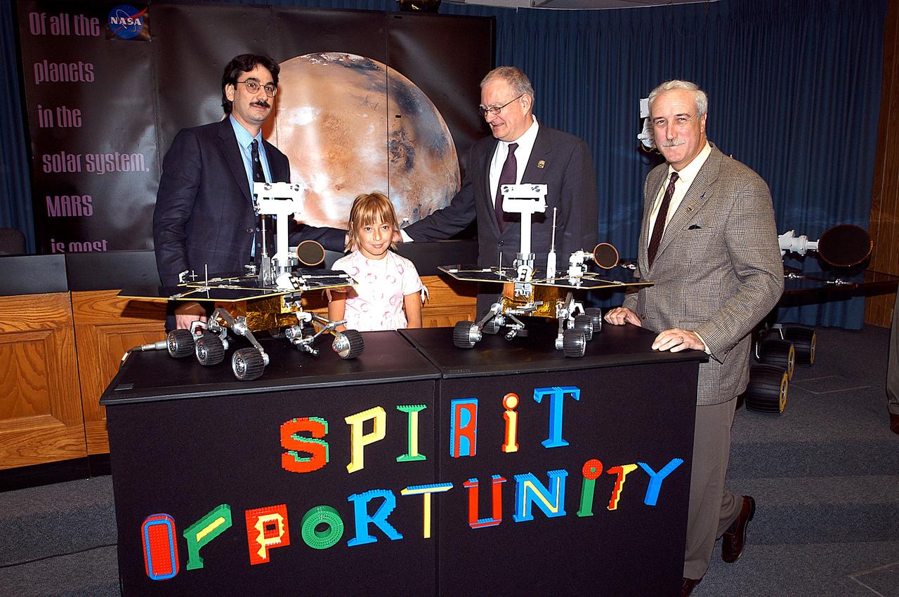 KENNEDY SPACE CENTER, FLA. -  Nine-year-old Sofi Collis poses proudly with a banner displaying the names she selected for the Mars Exploration Rovers -- "Spirit" and "Opportunity" -- during a press conference. Participating in the press conference are, from left, Brad Justus, LEGO Co. senior vice president; Sofi Collis, a third grade student from Arizona; Dr. John Marburger, science advisor to the President and director of the Office of Science and Technology Policy; and NASA Administrator Sean O'Keefe. The names Sofi suggested were selected from more than 10,000 student entries in an essay contest managed for NASA by the LEGO Company. NASA's twin Mars Exploration Rovers are designed to study the history of water on Mars. These robotic geologists are equipped with a robotic arm, a drilling tool, three spectrometers, and four pairs of cameras that allow them to have a human-like, 3D view of the terrain. Each rover could travel as far as 100 meters in one day to act as Mars scientists' eyes and hands, exploring an environment where humans are not yet able to go. MER-A, with the rover Spirit aboard, is scheduled to launch on June 8 at 2:06 p.m. EDT, with two launch opportunities each day during a launch period that closes on June 24.