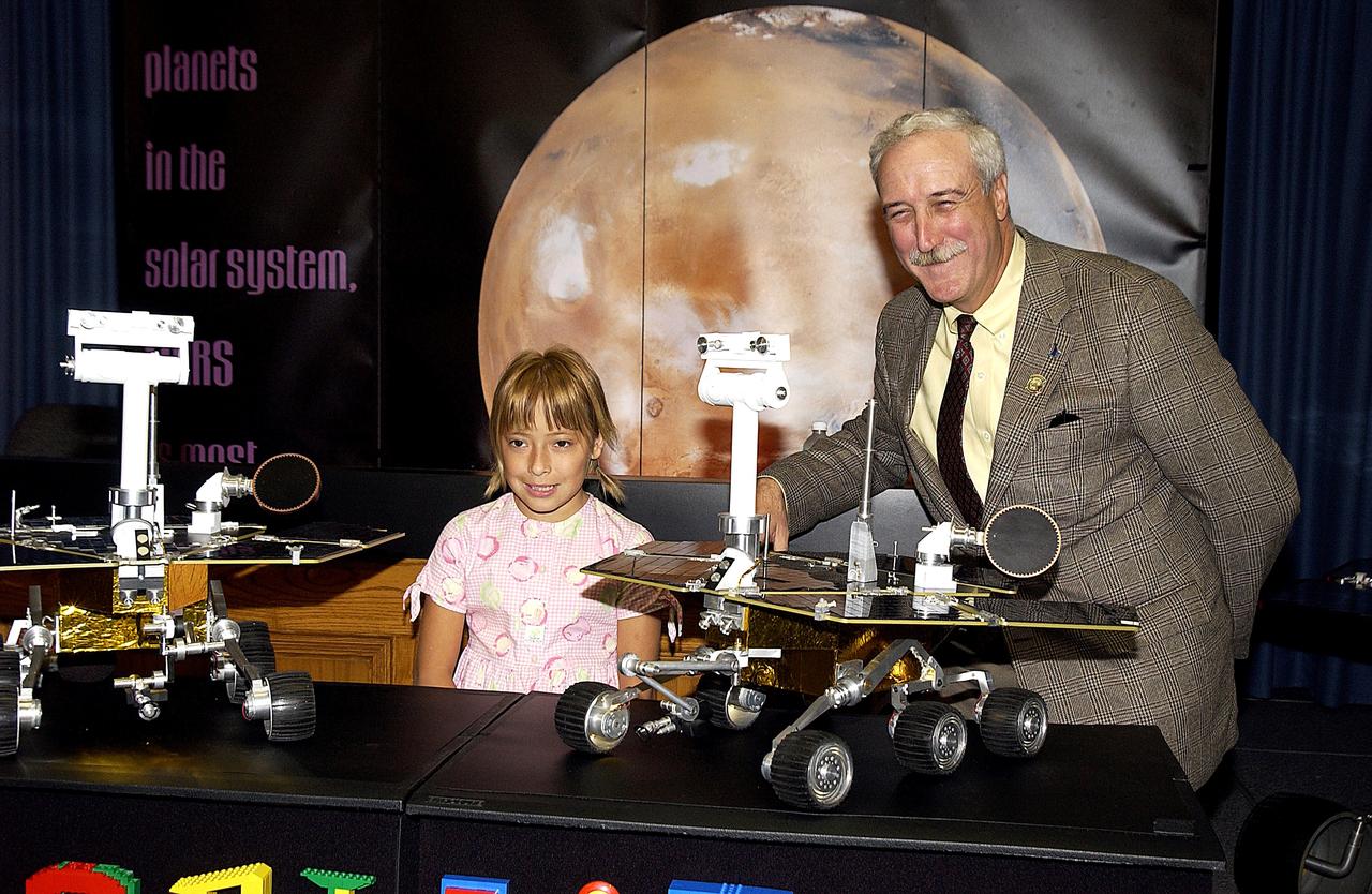 KENNEDY SPACE CENTER, FLA. -  Nine-year-old Sofi Collis (left) is introduced to the media by NASA Administrator Sean O'Keefe at a press conference.   The Siberian-born Arizona resident wrote the winning entry in the Name the Rovers Contest sponsored by NASA and the Lego Co., a Denmark-based toymaker, with collaboration from the Planetary Society, Pasadena, Calif.  The names she selected for the Mars Exploration Rovers are "Spirit" and "Opportunity." The third grader's essay was chosen from more than 10,000 American student entries.  NASA's twin Mars Exploration Rovers are designed to study the history of water on Mars. These robotic geologists are equipped with a robotic arm, a drilling tool, three spectrometers, and four pairs of cameras that allow them to have a human-like, 3D view of the terrain. Each rover could travel as far as 100 meters in one day to act as Mars scientists' eyes and hands, exploring an environment where humans are not yet able to go. MER-A, with the rover Spirit aboard, is scheduled to launch on June 8 at 2:06 p.m. EDT, with two launch opportunities each day during a launch period that closes on June 24.