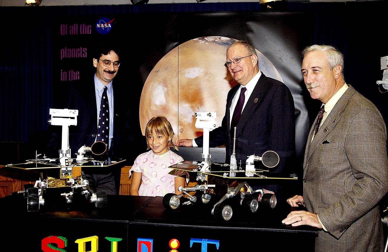 KENNEDY SPACE CENTER, FLA. -  Nine-year-old Sofi Collis poses proudly with a banner displaying the names she selected for the Mars Exploration Rovers -- "Spirit" and "Opportunity" -- during a press conference. Participating in the press conference are, from left, Brad Justus, LEGO Co. senior vice president; Sofi Collis, third grade student from Arizona; Dr. John Marburger, science advisor to the President and director of the Office of Science and Technology Policy; and NASA Administrator Sean O'Keefe. The names Sofi suggested were selected from more than 10,000 student entries in an essay contest managed for NASA by the LEGO Company. NASA's twin Mars Exploration Rovers are designed to study the history of water on Mars. These robotic geologists are equipped with a robotic arm, a drilling tool, three spectrometers, and four pairs of cameras that allow them to have a human-like, 3D view of the terrain. Each rover could travel as far as 100 meters in one day to act as Mars scientists' eyes and hands, exploring an environment where humans are not yet able to go. MER-A, with the rover Spirit aboard, is scheduled to launch on June 8 at 2:06 p.m. EDT, with two launch opportunities each day during a launch period that closes on June 24.
