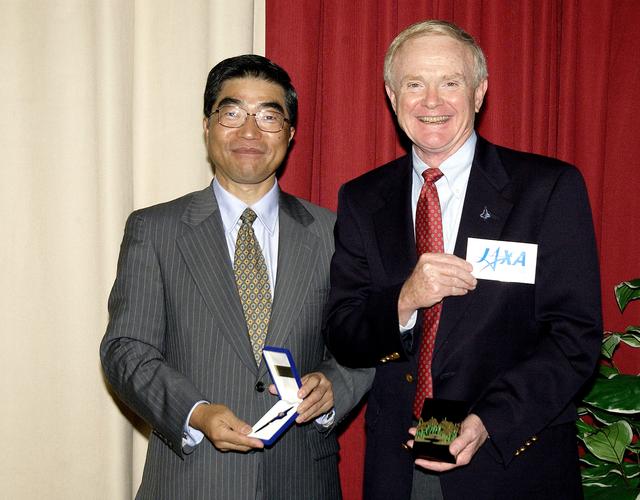 KENNEDY SPACE CENTER, FLA. -  Executive Director of NASDA Koji Yamamoto (left) and Center Director Roy Bridges Jr. (right) exchange mementos during Mr. Yamamoto’s visit to KSC.  Mr. Bridges also holds the logo of the new Japan Aerospace Exploration Agency, a merger of three Japanese aeronautical and space agencies effective Oct.1, 2003.  Mr. Yamamoto is at KSC for a welcome ceremony involving the arrival of the newest Space Station module, the Japanese Experiment Module/pressurized module.  His visit includes a tour of the Columbia Debris Hangar.