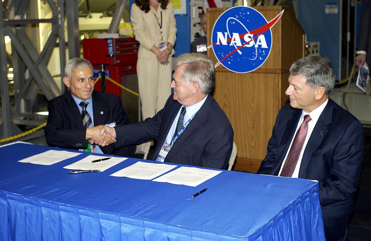 KENNEDY SPACE CENTER, FLA. - At ceremony highlighting the arrival of two major components of the International Space Station, Node 2 and the Japanese Experiment Module (JEM), ownership of Node 2 was officially transferred between the European Space Agency and NASA.  Shaking hands after the signing are Andrea Lorenzoni, International Space Station Program manager for Node 2, Italian Space Agency; and Alan Thirkettle, International Space Station Program manager for Node 2, European Space Agency (ESA).  At right is NASA’s Michael C. Kostelnik, deputy associate administrator for International Space Station and Shuttle Programs.  NASA's Node 2, built by ESA in Italy, arrived at KSC on June 1. It will be the next pressurized module installed on the Station. The pressurized module of the Japanese Experiment Module (JEM),  named "Kibo" (Hope), arrived at KSC on June 4. It is Japan's primary contribution to the Station. Emceed by Lisa Malone, deputy director of External Relations and Business Development at KSC, the ceremony also included these speakers: Center Director Roy Bridges Jr.; NASA’s William Gerstenmaier, International Space Station Program manager; and Kuniaki Shiraki, JEM Project manager, National Aerospace and Development Agency of Japan.