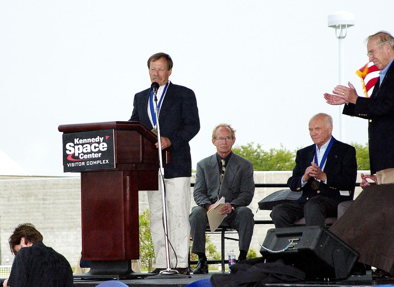 KENNEDY SPACE CENTER, FLA. -  At the KSC Visitor Complex, former astronaut Robert "Hoot" Gibson (at podium) addresses the audience at his induction ceremony into the U.S. Astronaut Hall of Fame. Also standing is former astronaut James A. Lovell.  Seated on the dais, from left, are actor and Master of Ceremonies Lance Henriksen and former astronaut John H. Glenn.  Also being inducted with Gibson are Space Shuttle astronauts Daniel Brandenstein, Story Musgrave, and Sally K. Ride. Conceived by six of the Mercury Program astronauts, the U.S. Astronaut Hall of Fame opened in 1990 to provide a place where space travelers could be remembered for their participation and accomplishments in the U.S. space program. The four new inductees join 48 previously honored astronauts from the ranks of the Gemini, Apollo, Skylab, Apollo-Soyuz, and Space Shuttle programs.