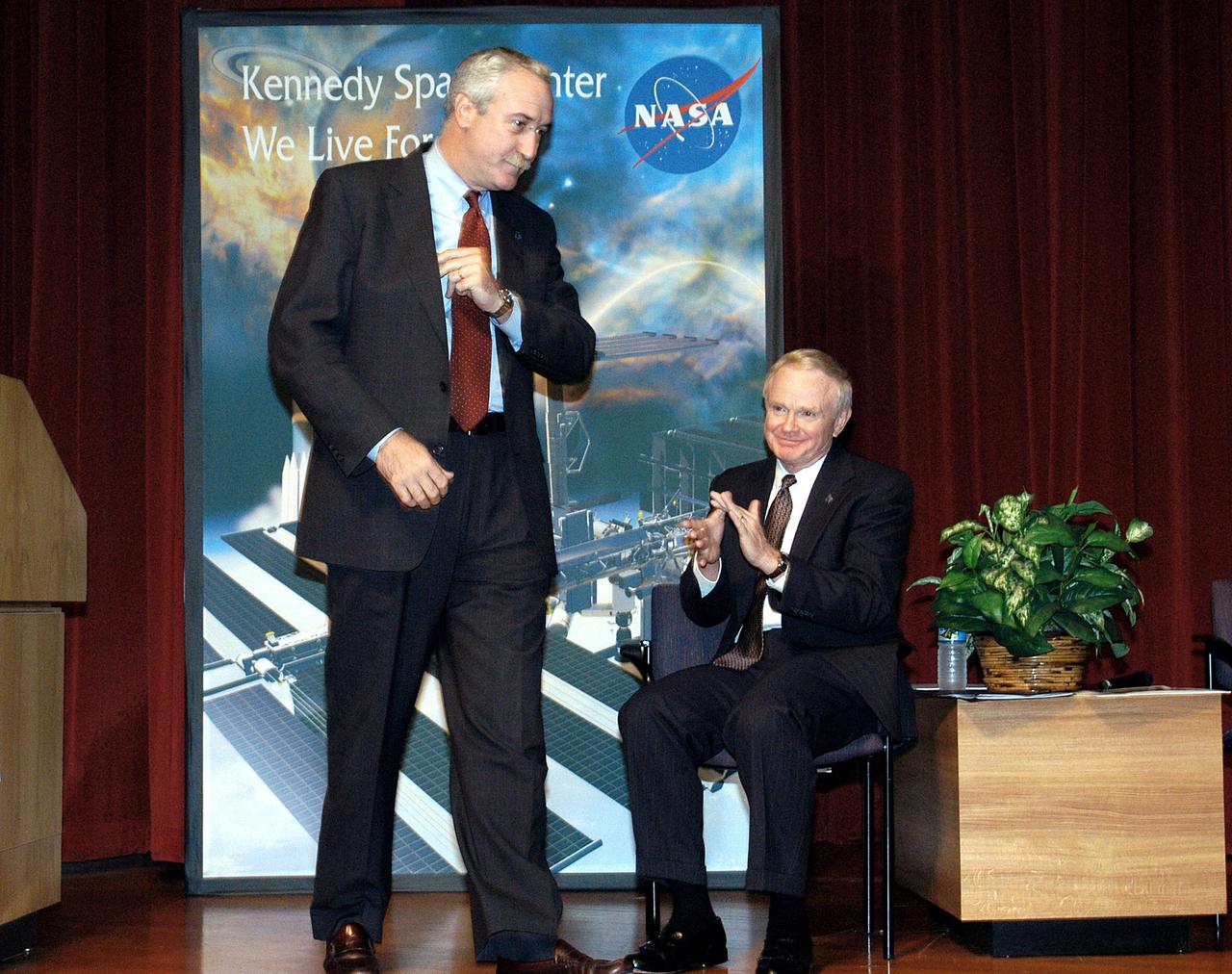 KENNEDY SPACE CENTER, FLA. -  NASA Administrator Sean O'Keefe (left) receives the applause of KSC Director Roy D. Bridges (right) and a group of KSC employees assembled in the KSC Training Auditorium.  The occasion is the announcement of James W. Kennedy as the next director of the NASA Kennedy Space Center (KSC) in Florida. Kennedy has served as KSC's deputy director since November 2002. He will succeed Bridges, who was appointed on June 13 to lead NASA's Langley Research Center, Hampton, Va.