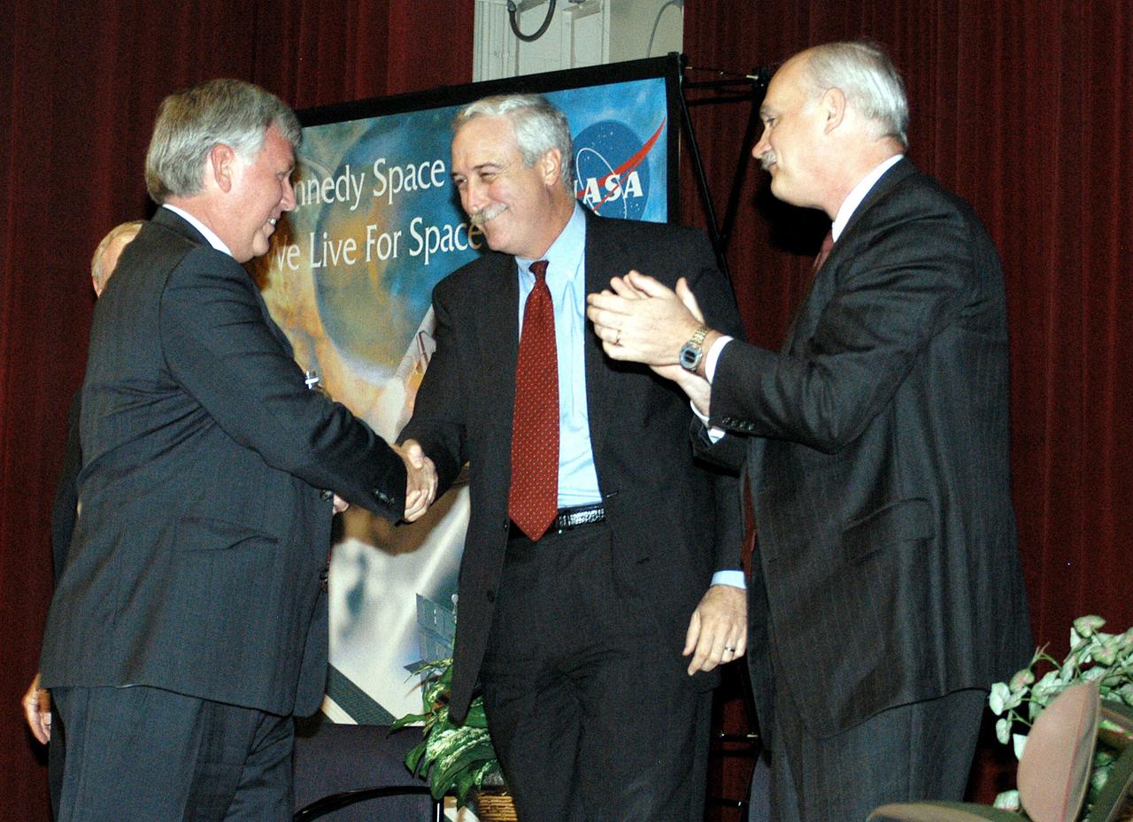 KENNEDY SPACE CENTER, FLA. -  KSC Deputy Director James W. Kennedy (left) and NASA Administrator Sean O'Keefe shake hands before a group of KSC employees assembled in the KSC Training Auditorium.  NASA Associate Administrator for Space Flight William F. Readdy applauds, at right. The occasion is the announcement of Kennedy as the next director of the NASA Kennedy Space Center (KSC) in Florida. Kennedy has served as KSC's deputy director since November 2002. He will succeed KSC Director Roy D. Bridges, who was appointed on June 13 to lead NASA's Langley Research Center, Hampton, Va.
