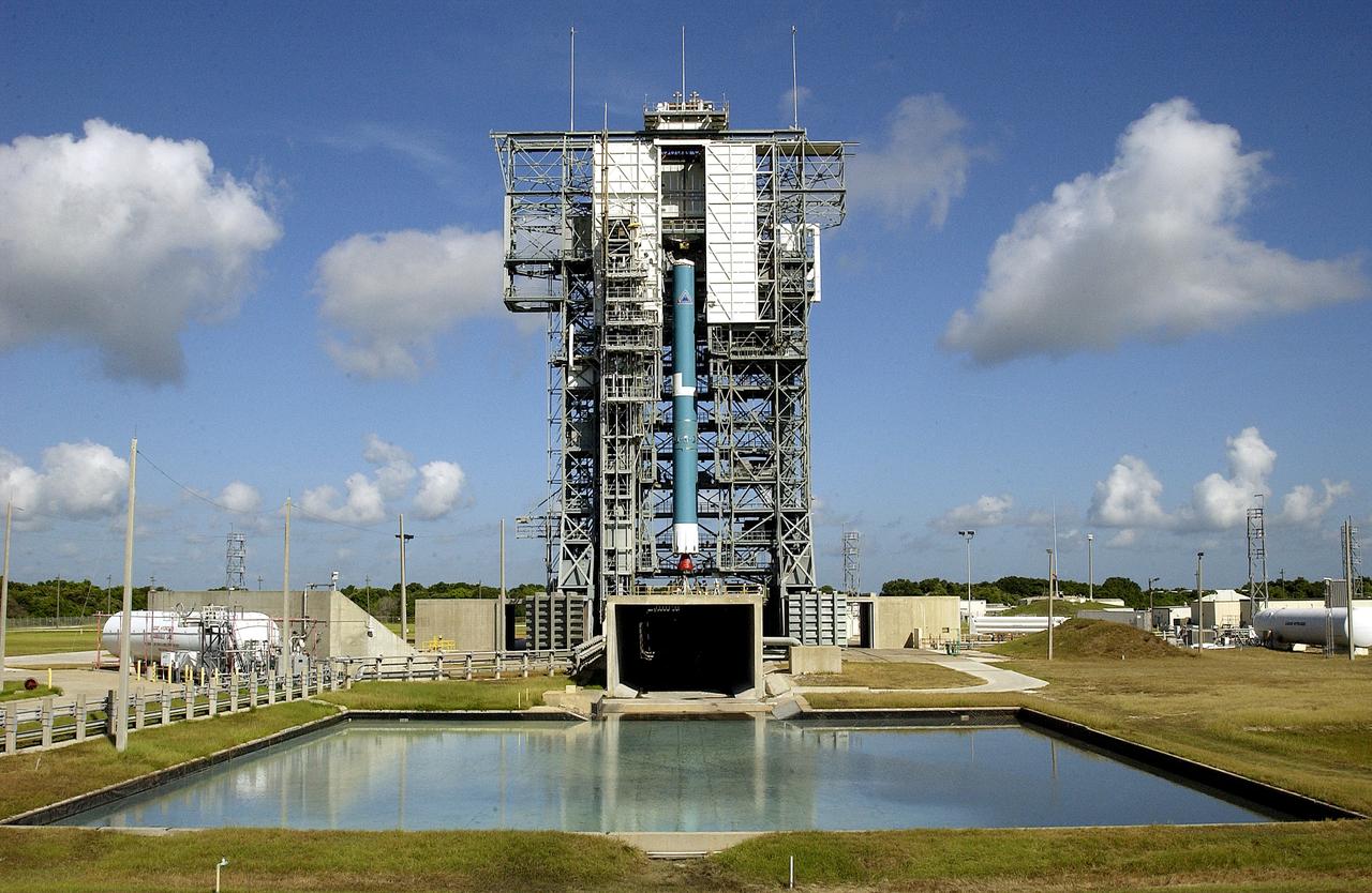 KENNEDY SPACE CENTER, FLA. - On Launch Complex 17-B, Cape Canaveral Air Force Station, the first stage of a Delta II rocket is lifted up the mobile service tower. Below the rocket is the flame trench, and in the foreground is the overflow pool. The rocket is being erected to launch the Space InfraRed Telescope Facility (SIRTF). Consisting of an 0.85-meter telescope and three cryogenically cooled science instruments, SIRTF is one of NASA's largest infrared telescopes to be launched. SIRTF will obtain images and spectra by detecting the infrared energy, or heat, radiated by objects in space. Most of this infrared radiation is blocked by the Earth's atmosphere and cannot be observed from the ground.