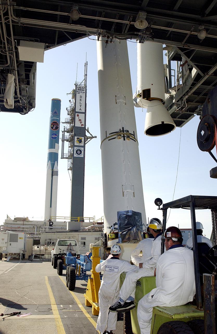 KENNEDY SPACE CENTER, FLA. -   Another solid rocket booster (SRB) is lifted to vertical on Launch Complex 17-B, Cape Canaveral Air Force Station, to join the one already in place in the mobile service tower.  The SRBs will be attached to the Delta II Heavy rocket in the background that will launch the Space Infrared Telescope Facility (SIRTF). The Delta II Heavy features nine 46-inch-diameter, stretched SRBs.  SIRTF, consisting of three cryogenically cooled science instruments and an 0.85-meter telescope, is one of NASA's largest infrared telescopes to be launched.  SIRTF will obtain images and spectra by detecting the infrared energy, or heat, radiated by objects in space. Most of this infrared radiation is blocked by the Earth's atmosphere and cannot be observed from the ground.