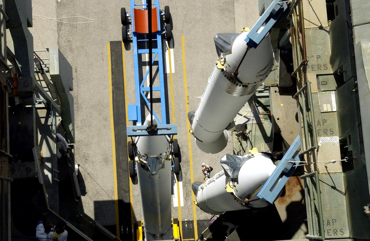 KENNEDY SPACE CENTER, FLA. - This view from the mobile service tower on Launch Complex 17-B, Cape Canaveral Air Force Station, shows two solid rocket boosters (SRBs) already suspended in the tower while another is being lifted. They are three of nine 46-inch-diameter, stretched SRBs that are being attached to the Delta II Heavy rocket that will launch the Space Infrared Telescope Facility (SIRTF). Consisting of three cryogenically cooled science instruments and an 0.85-meter telescope, SIRTF is one of NASA's largest infrared telescopes to be launched. SIRTF will obtain images and spectra by detecting the infrared energy, or heat, radiated by objects in space. Most of this infrared radiation is blocked by the Earth's atmosphere and cannot be observed from the ground.