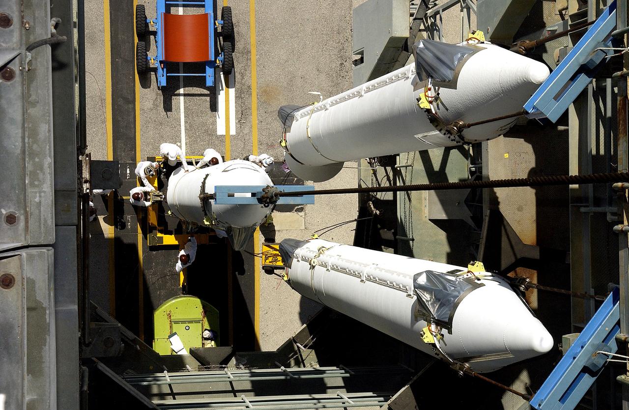 KENNEDY SPACE CENTER, FLA. - This view from the mobile service tower on Launch Complex 17-B, Cape Canaveral Air Force Station, shows two solid rocket boosters (SRBs) already suspended in the tower while another is being lifted. They are three of nine 46-inch-diameter, stretched SRBs that are being attached to the Delta II Heavy rocket that will launch the Space Infrared Telescope Facility (SIRTF). Consisting of three cryogenically cooled science instruments and an 0.85-meter telescope, SIRTF is one of NASA's largest infrared telescopes to be launched. SIRTF will obtain images and spectra by detecting the infrared energy, or heat, radiated by objects in space. Most of this infrared radiation is blocked by the Earth's atmosphere and cannot be observed from the ground.
