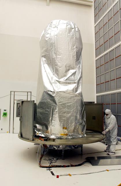 NASA image: KENNEDY SPACE CENTER, FLA.  -  A worker at Hangar A&E, Cape Canaveral Air Force Station, place the lower panels of the canister around the Space Infrared Telescope Facility (SIRTF).  The spacecraft will be transported to Launch Complex 17-B for mating with its launch vehicle, the Delta II rocket.   SIRTF consists of three cryogenically cooled science instruments and an 0.85-meter telescope, and is one of NASA's largest infrared telescopes to be launched.  SIRTF will obtain images and spectra by detecting the infrared energy, or heat, radiated by objects in space. Most of this infrared radiation is blocked by the Earth's atmosphere and cannot be observed from the ground.